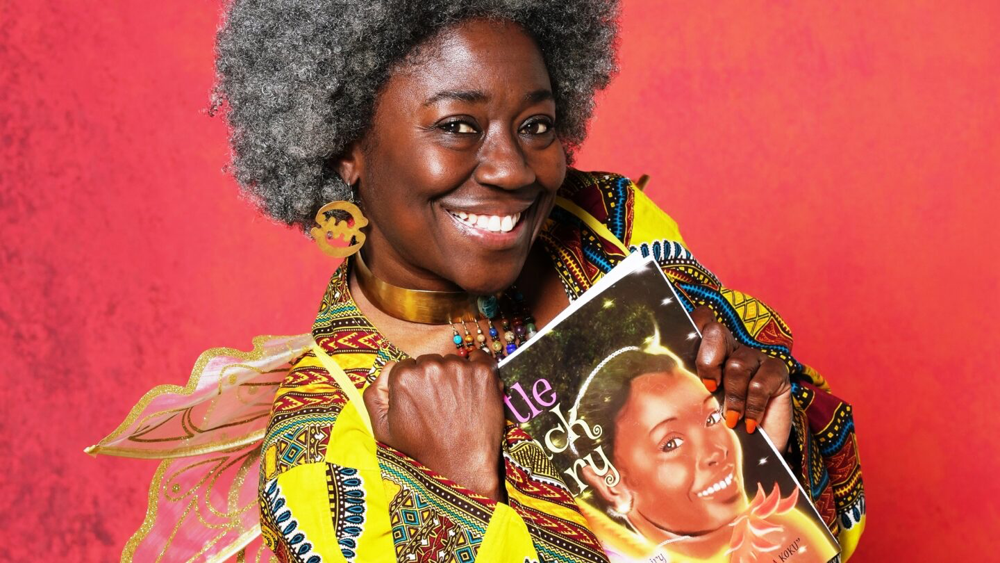Mama Koku holding her book against a vibrant red background